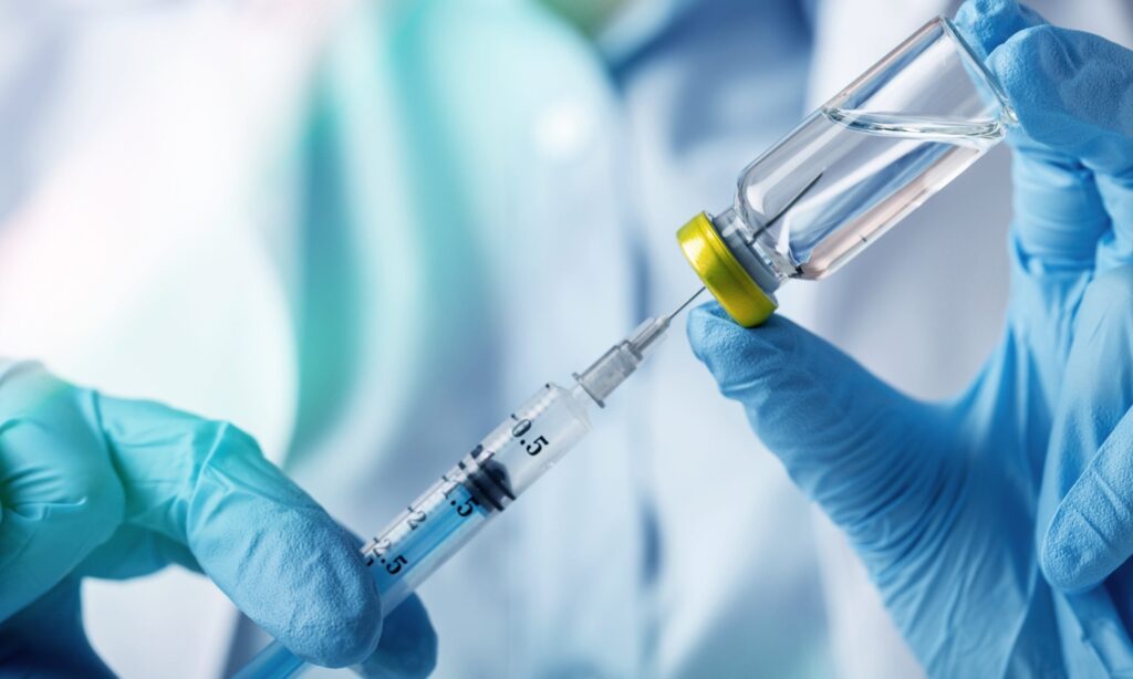 Doctor with latex gloves filling up a syringe with liquid.