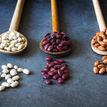 Three wooden spoons on a table that each have a different type of bean in them